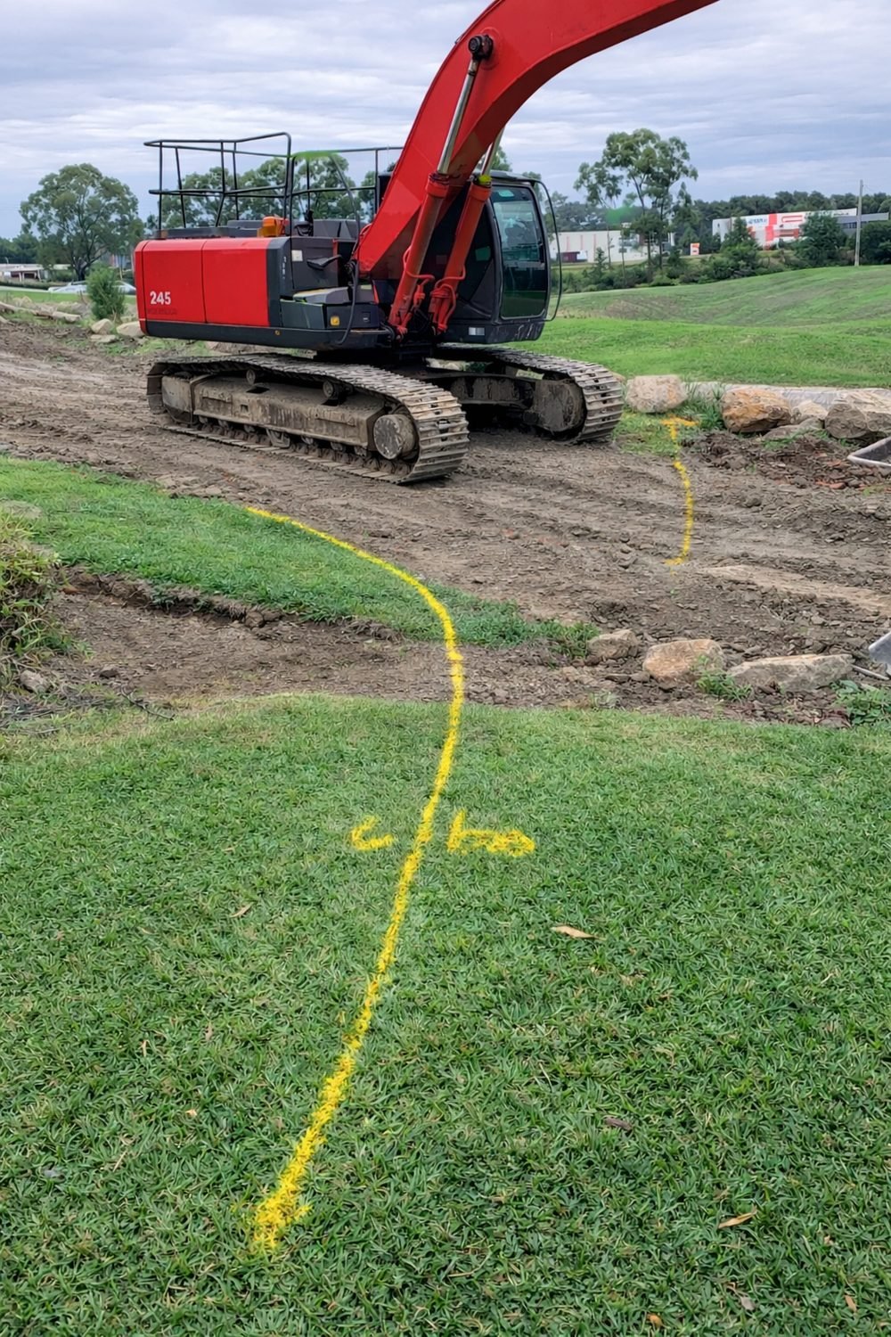 Yellow gas line marked across a lawn directly in front of a tracked excavator